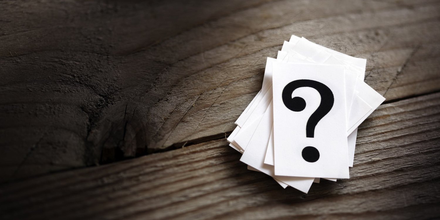 A stack of white cards with a black question mark on the top card, placed on a rustic wooden surface.