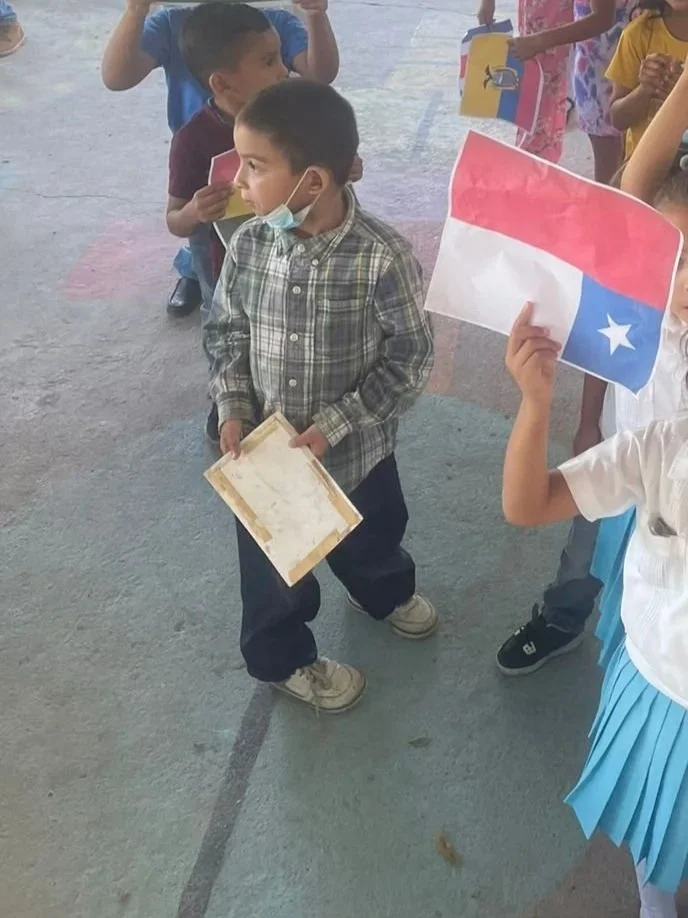 Children holding small flags of Texas at a school event.