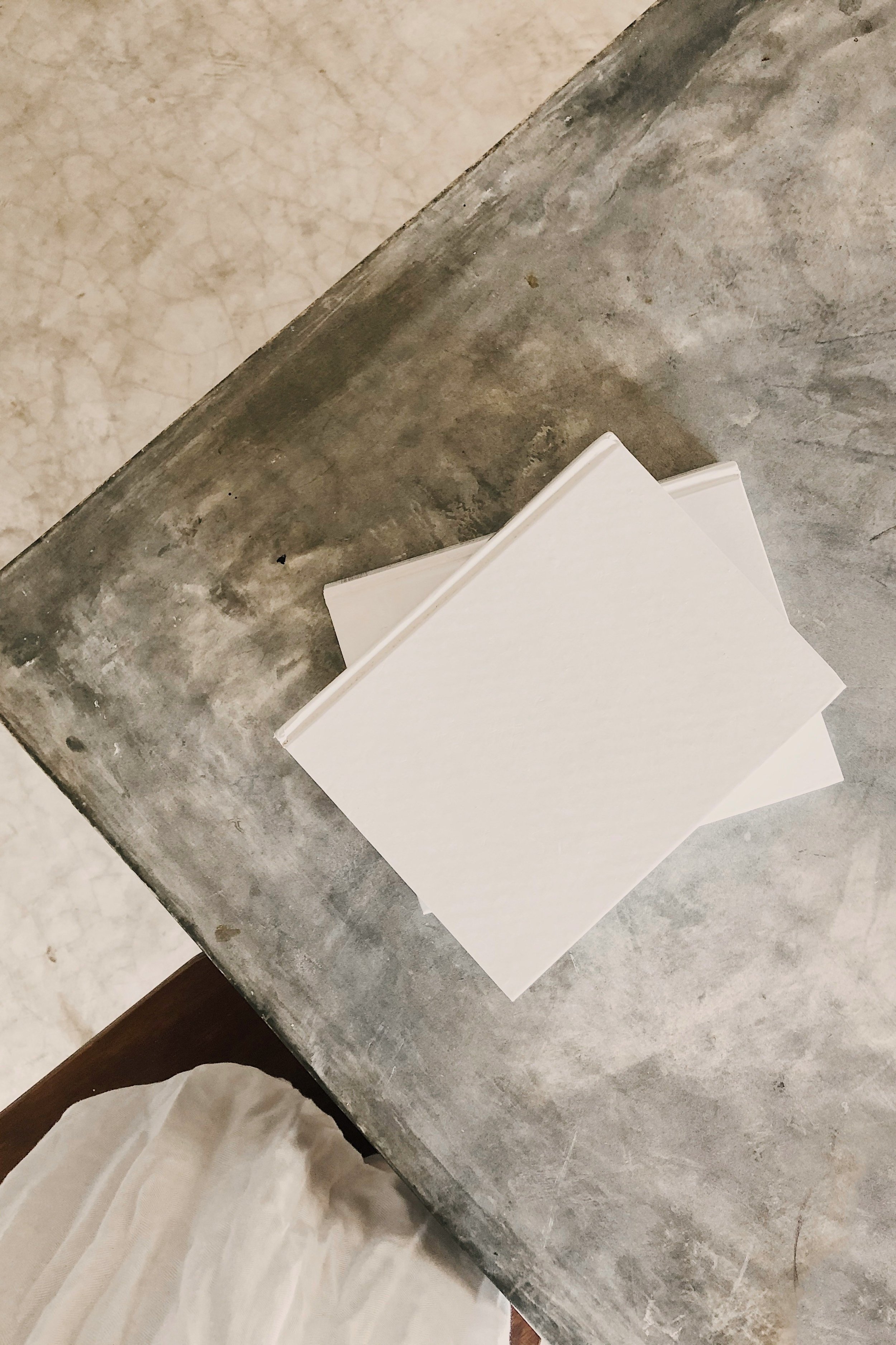 Close-up of a corner of a table with a textured gray surface, a section of parquet flooring, and some white papers on top. Part of a fingerless glove visible at the bottom.
