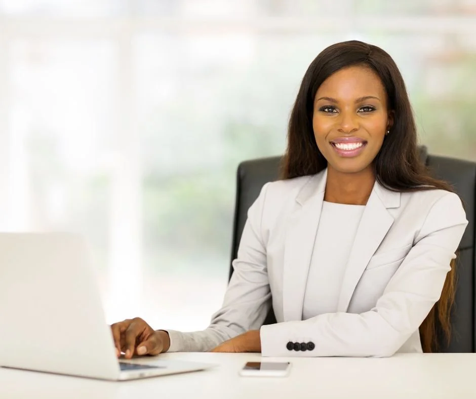 A professional woman sitting at a desk with a laptop and smile.