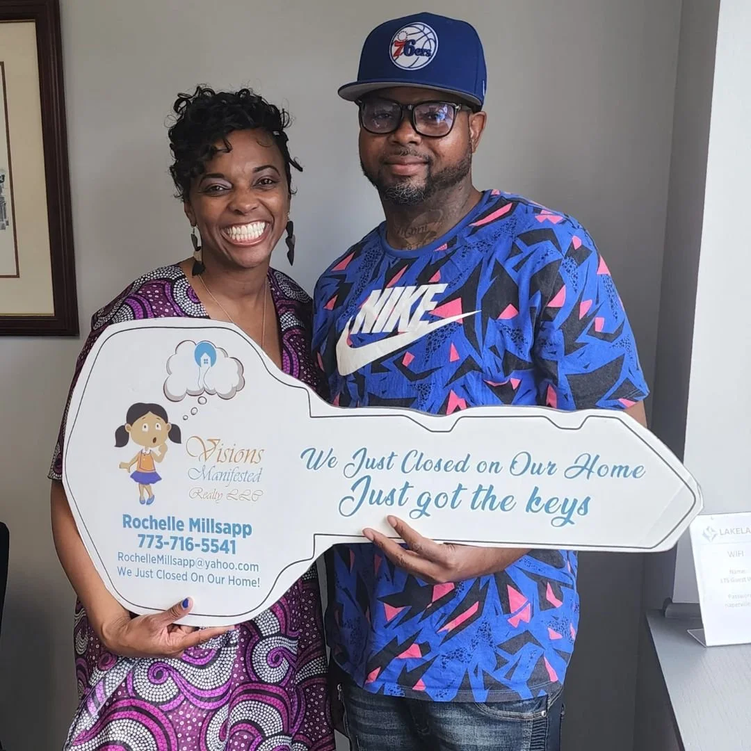 A woman and man smiling and holding a sign that says they just closed on their home and got the keys. The woman wears a purple patterned dress, and the man wears a blue Nike shirt and a Philadelphia 76ers cap.