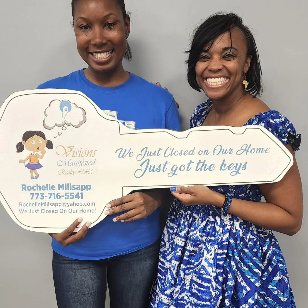 Two women smiling and holding a large key-shaped sign that says "We Just Closed on Our Home Just got the keys". The woman on the left is wearing a blue shirt, and the woman on the right is wearing a blue patterned dress.