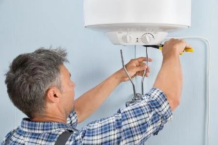 A man working on a white water heater mounted on a light blue wall.