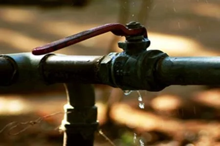 Close-up of a water pipe with a red handle tap, with water dripping from the outlet.