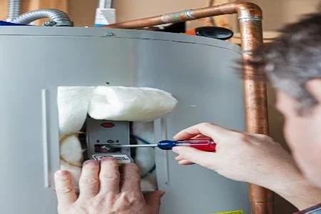 A person using a screwdriver to repair or maintain a furnace or water heater.