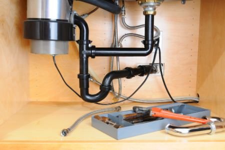 Under-sink plumbing with pipes, a toolbox, tools, and a wrench.