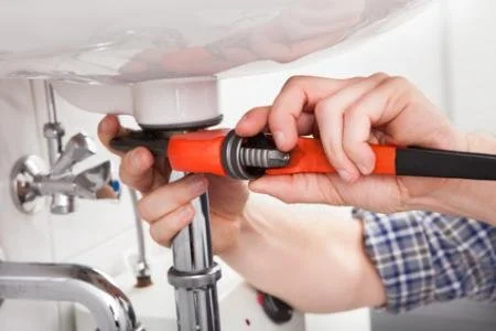 Person using a wrench to tighten a plumbing pipe under a sink.