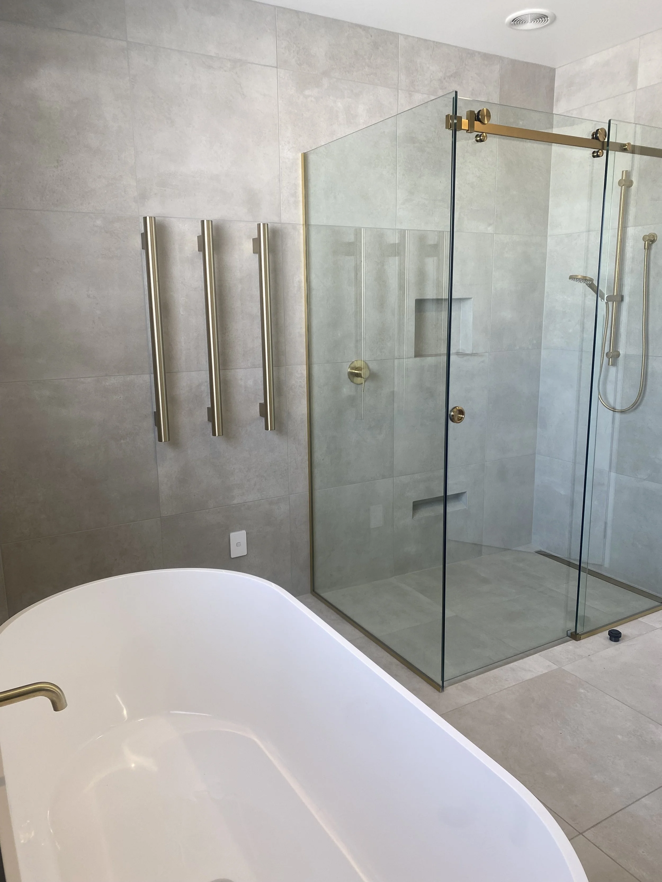 Modern bathroom with a glass shower enclosure, a built-in niche in the shower wall, a handheld showerhead, and a partial view of a white bathtub with a brass faucet.