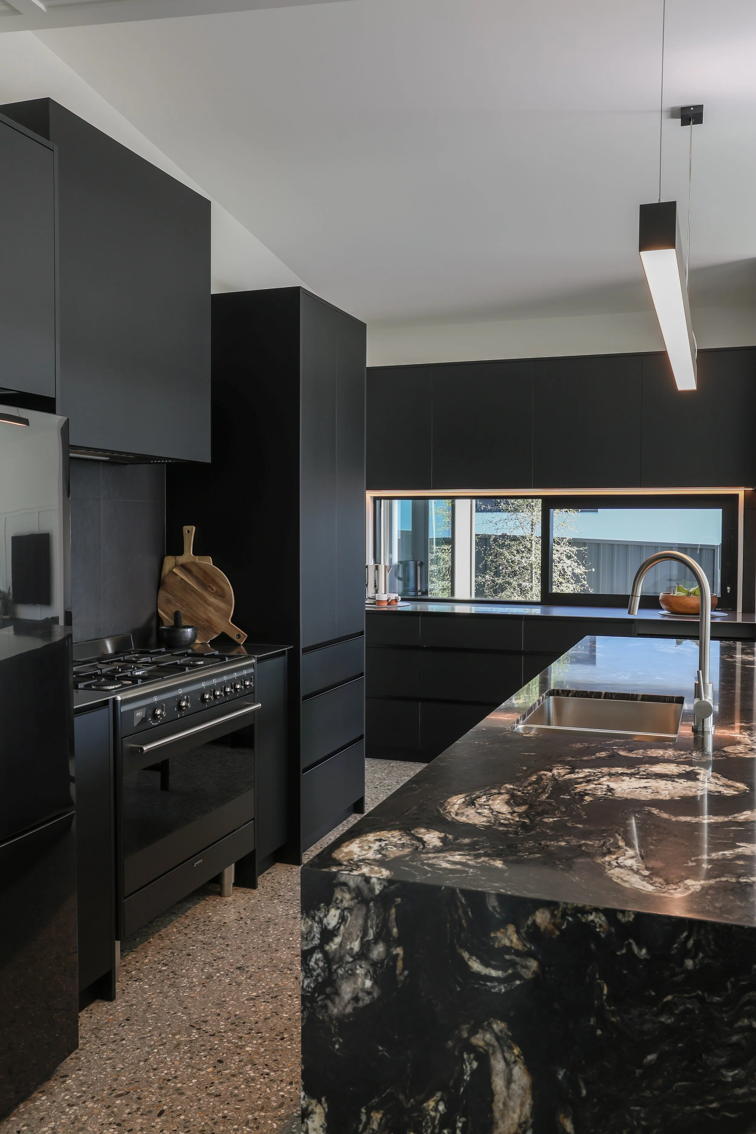 Modern kitchen with black cabinets, a gas stove, a marble countertop, and a window with a view of trees outside.