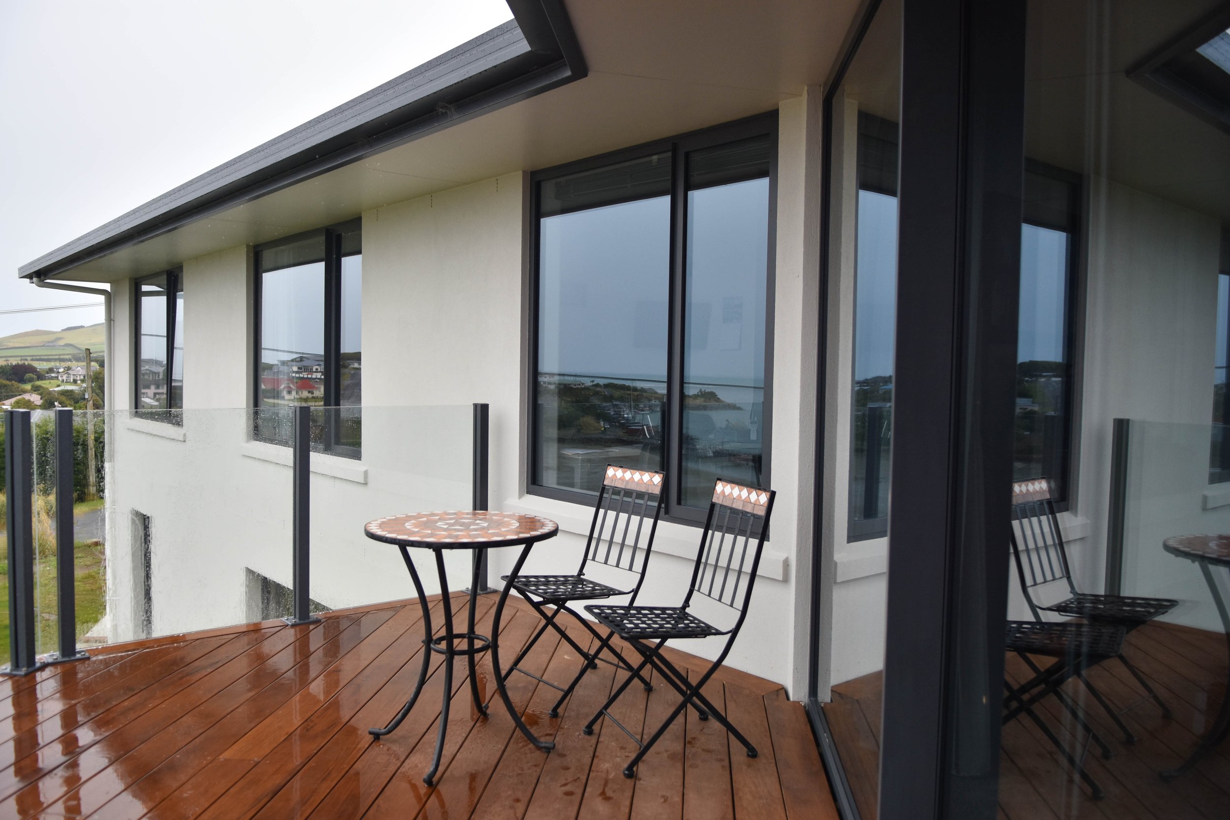 Balcony with a round table and two chairs, overlooking a view of a neighborhood with houses and hills in the distance.