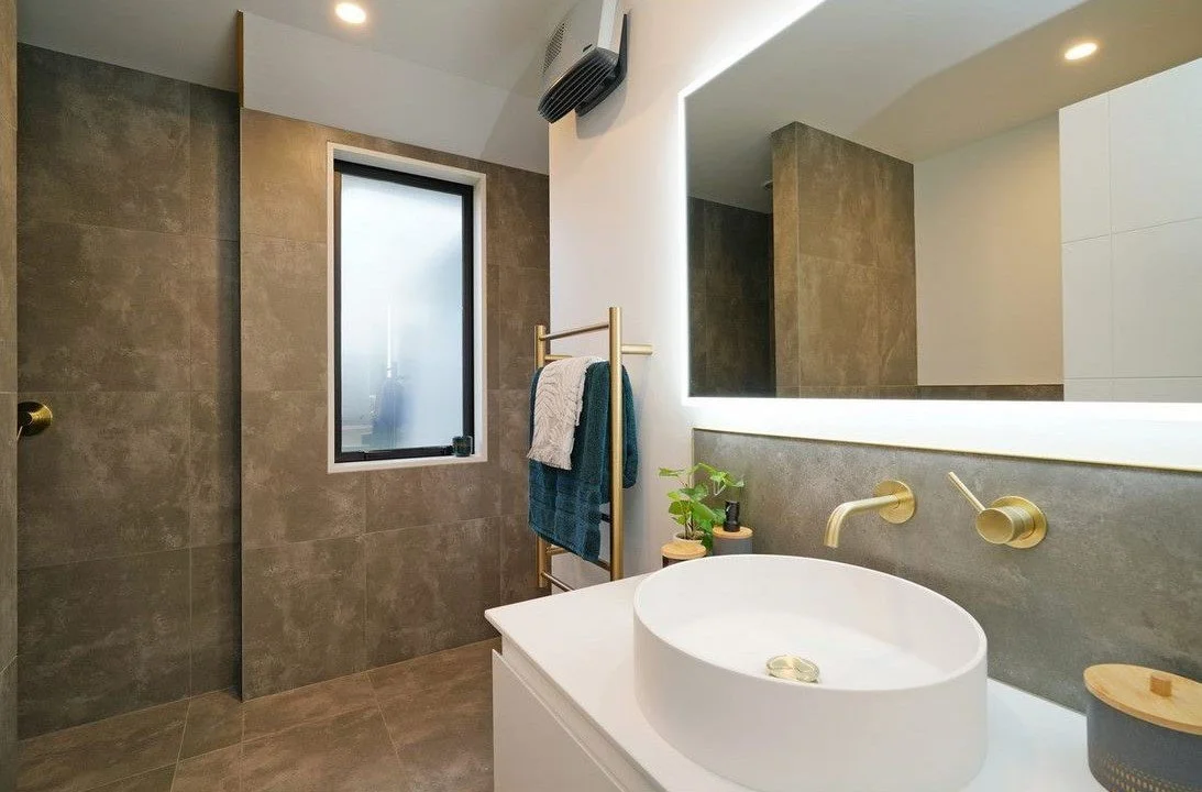 Modern bathroom with a round vessel sink, large mirror with backlighting, and a window with frosted glass.