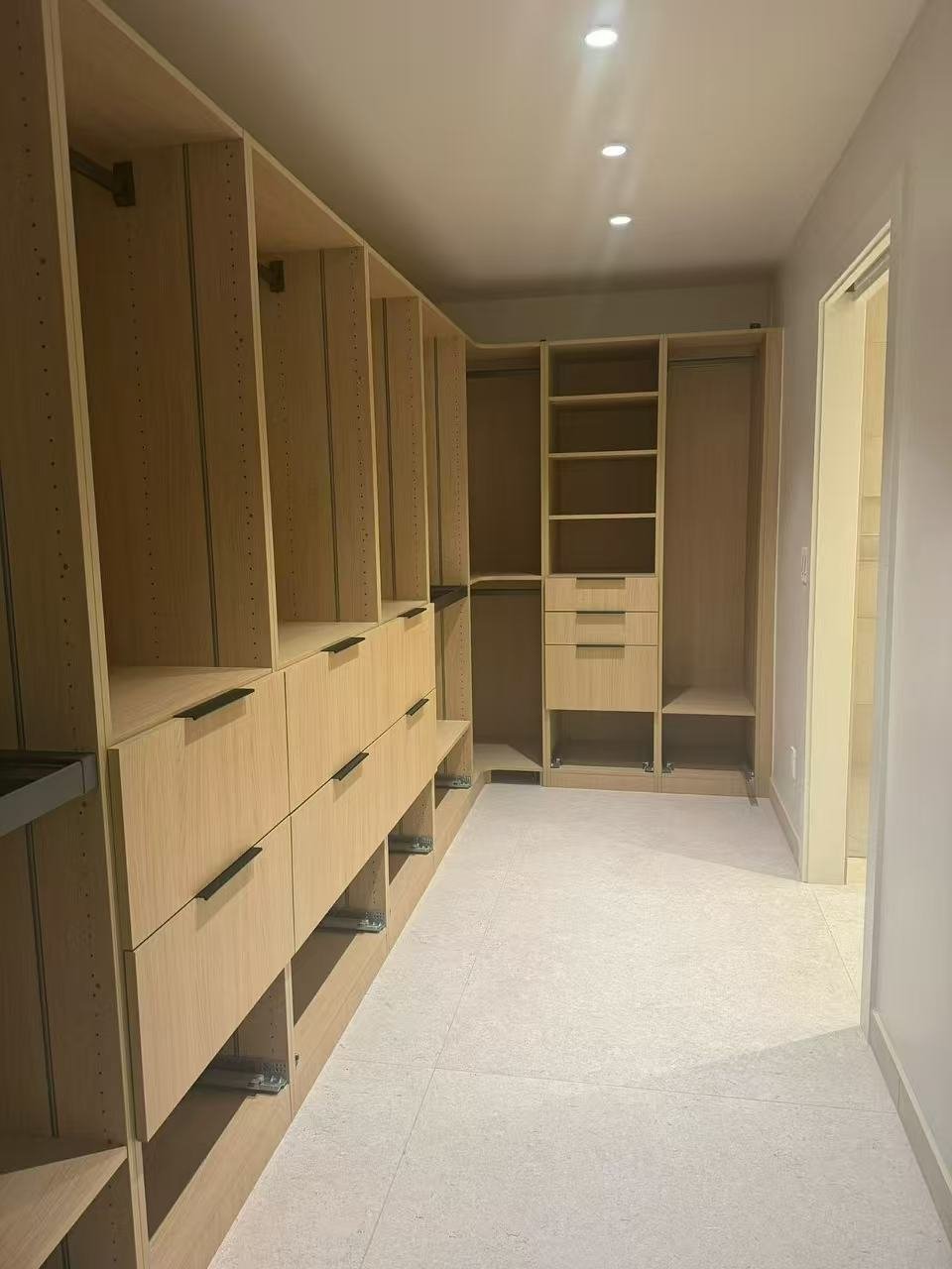 Empty walk-in closet with wooden shelving and drawers, illuminated by ceiling lights.