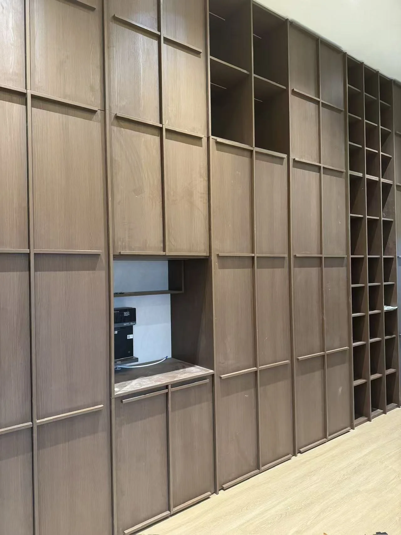 Empty wooden lockers with a small open compartment at the bottom, some containing electronic equipment, against a light-colored wall.