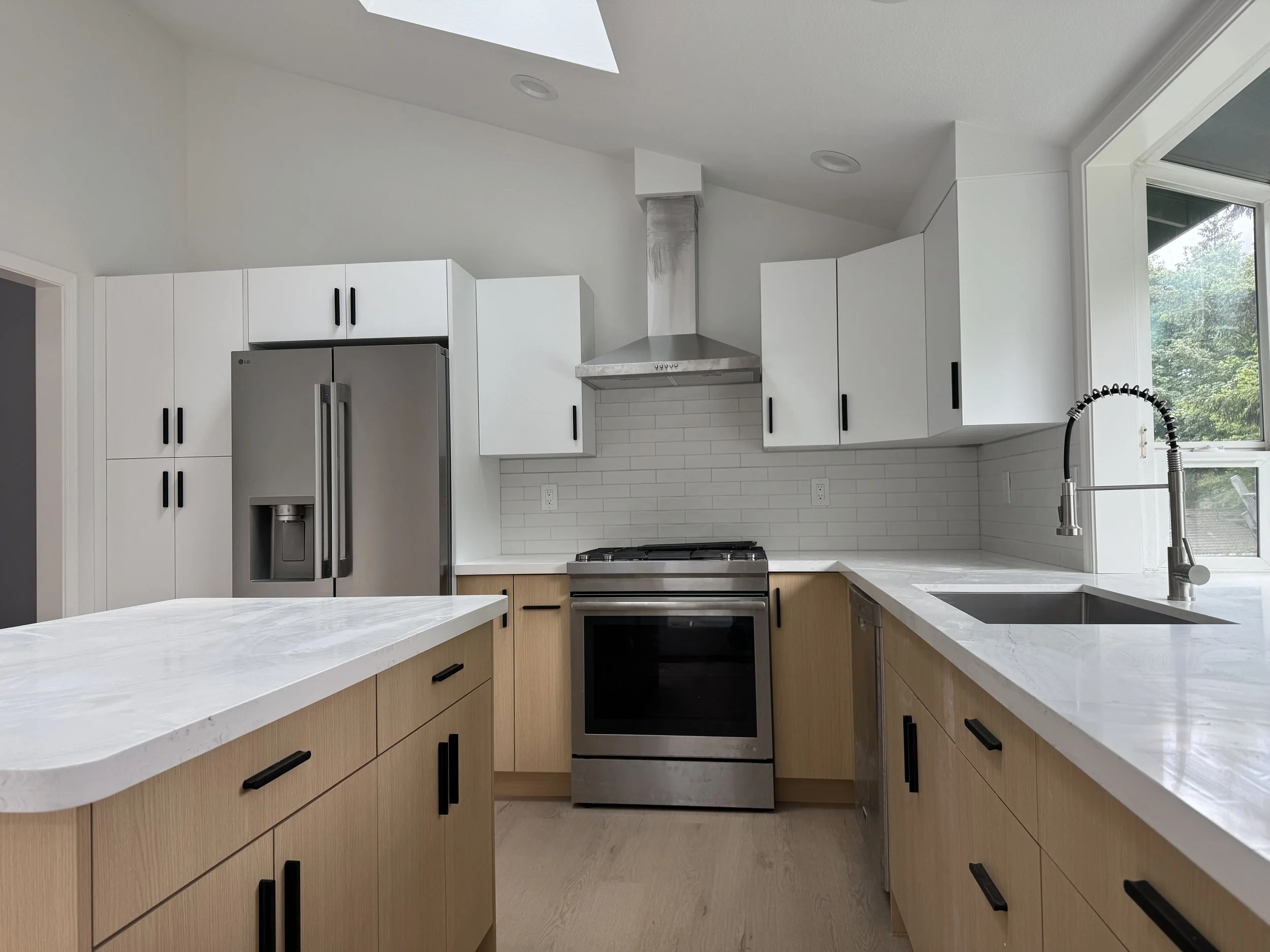 Modern kitchen with white cabinets, stainless steel appliances, a breakfast bar, a window, and a view of greenery outside.