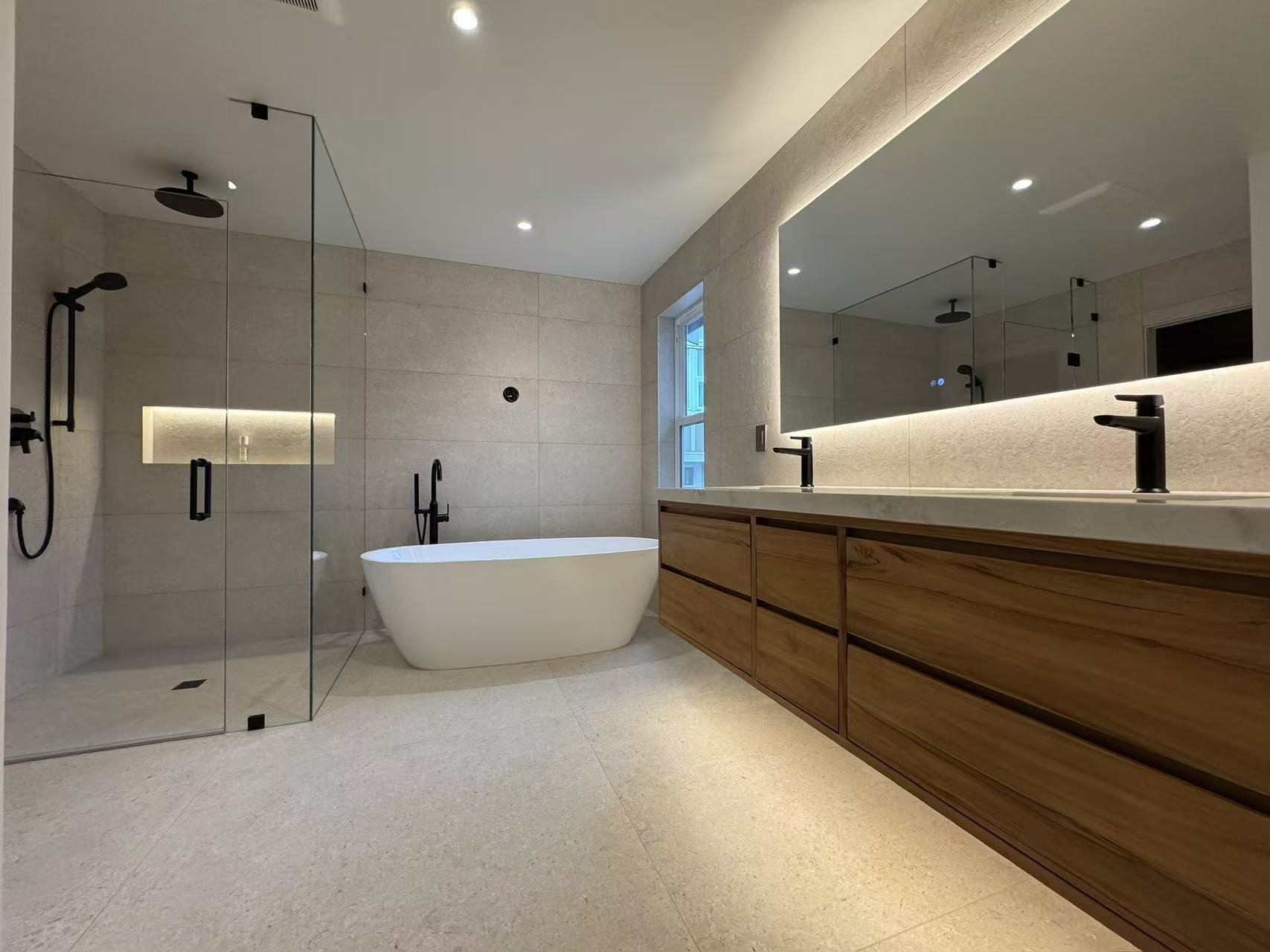 Modern bathroom with a large mirror, double sink vanity with wooden cabinets, freestanding bathtub, and a glass-enclosed shower area with black fixtures.