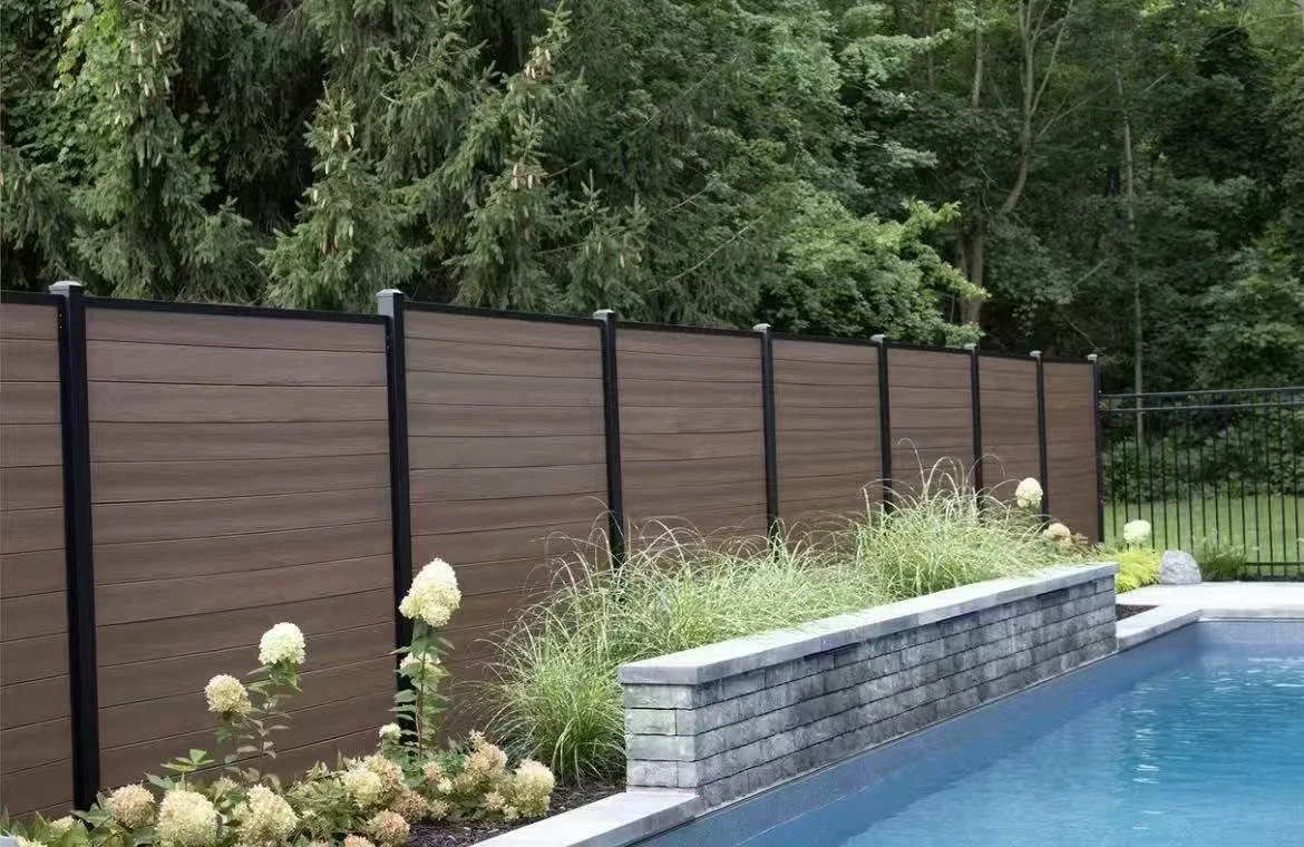 A backyard with a brown privacy fence, a swimming pool, and lush green trees in the background.