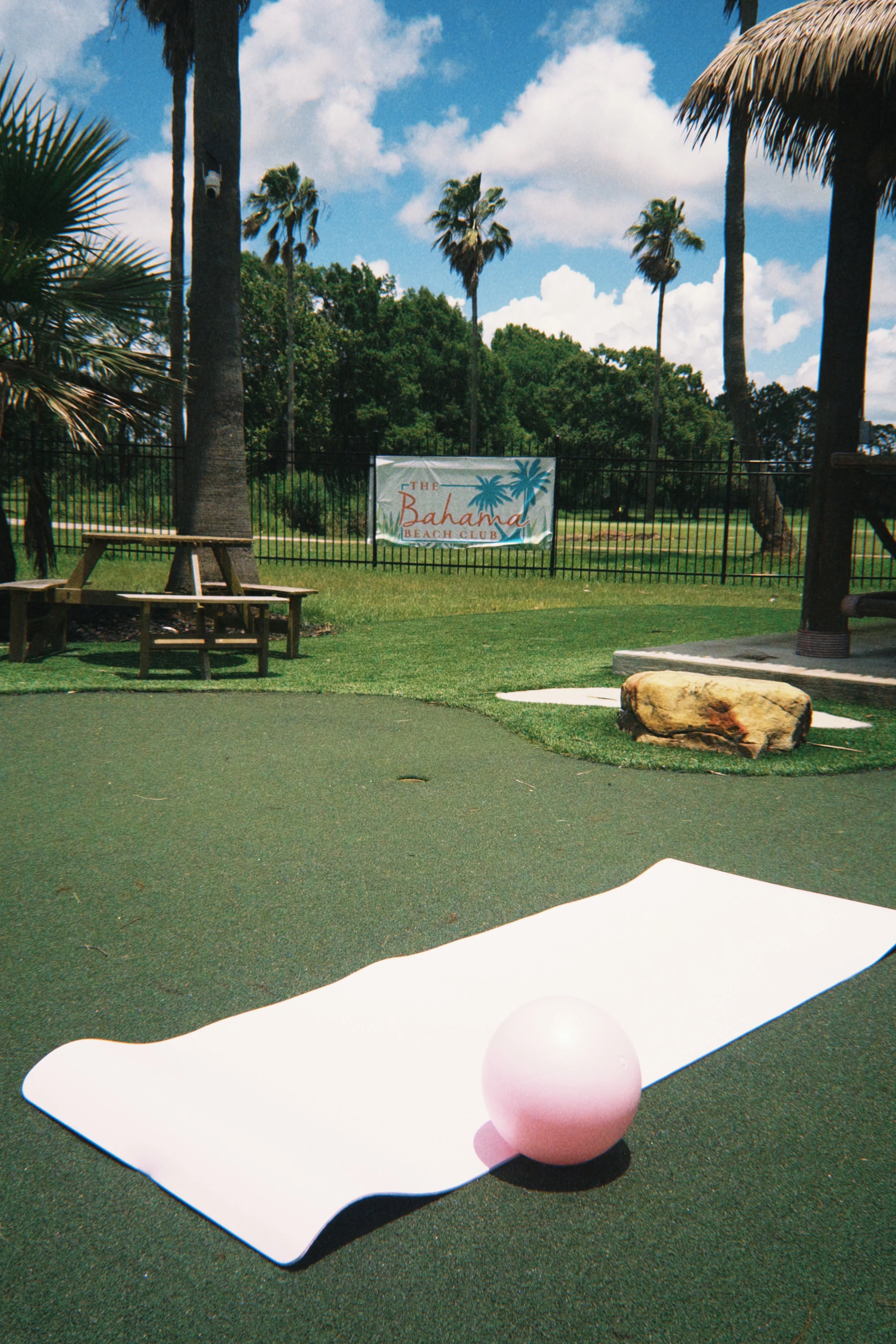 A pink ball resting on a pink, pilates mat in a golf course area with grass, trees, and a banner in the background that reads "The Bahamas Beach Club."
