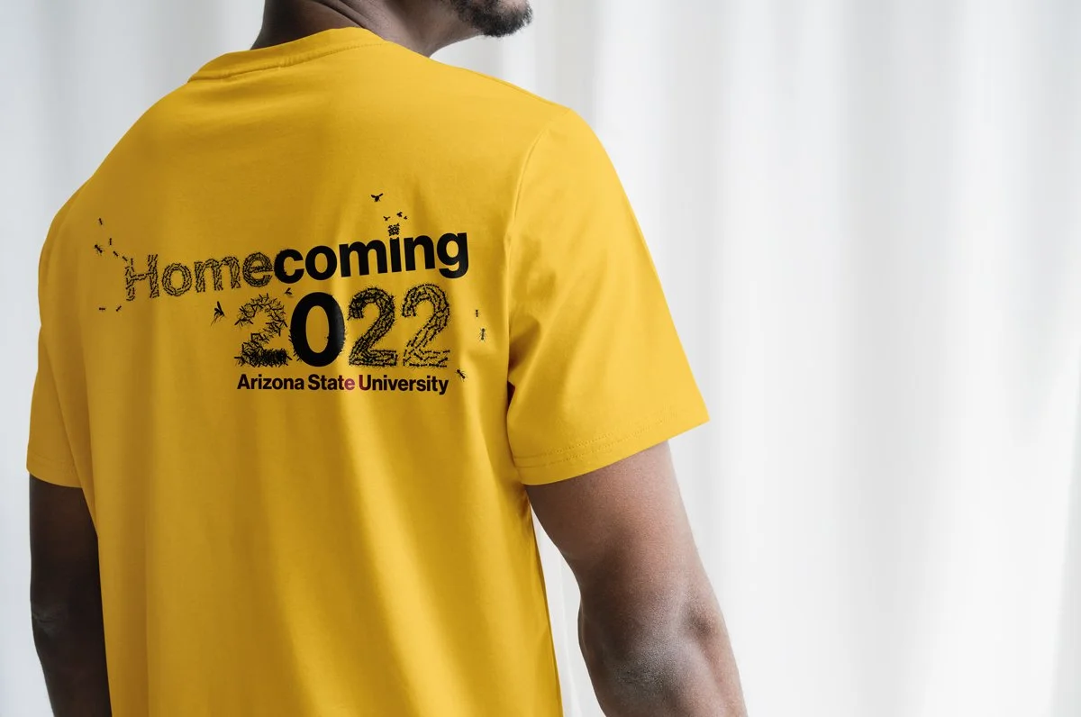 Man with his back to the camera wearing a gold t-shirt that reads Homecoming 2022.