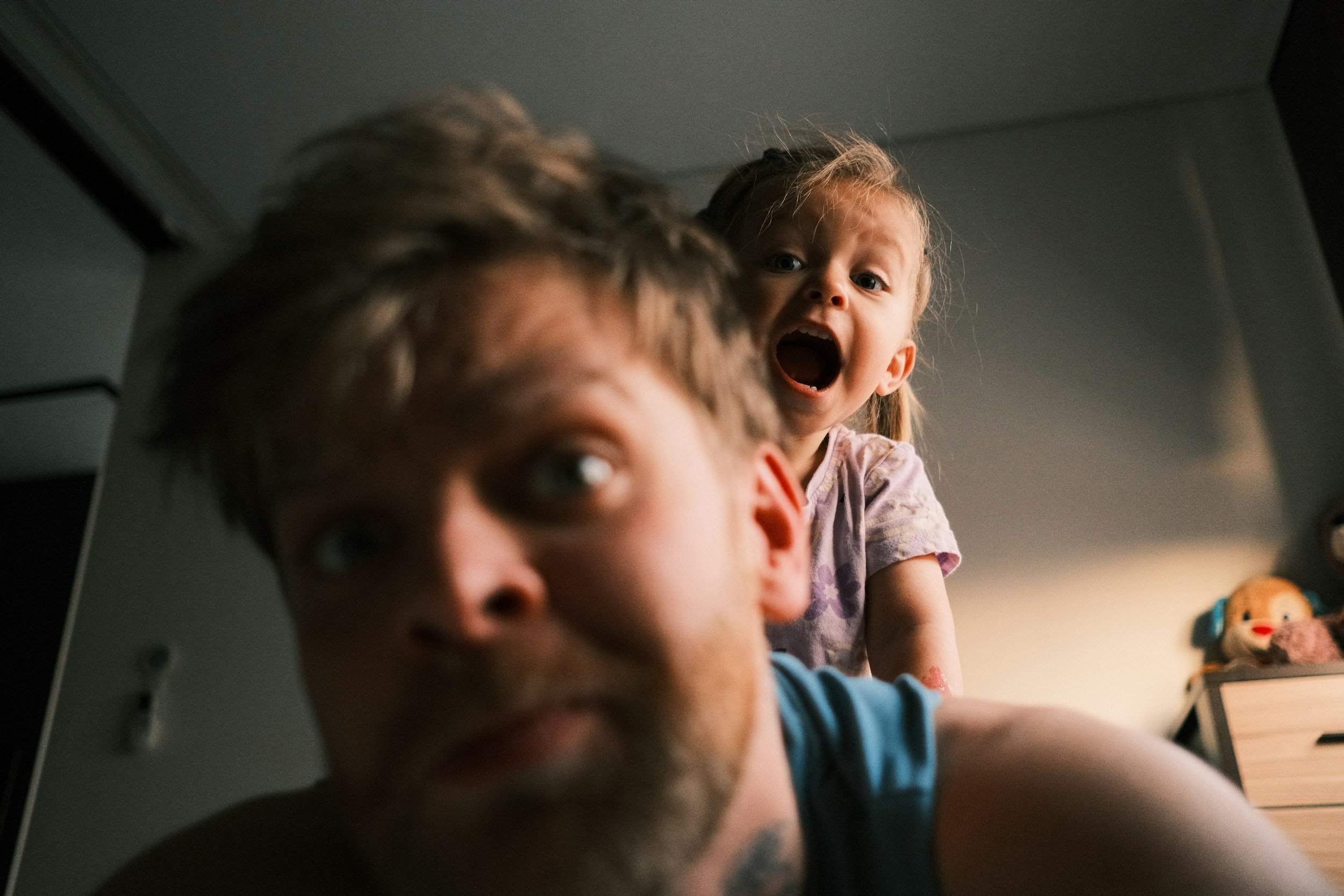 A girl with blonde hair and a girl with red hair is looking down at the camera with their mouths open, while a boy with brown hair is in the foreground with only part of his face visible.
