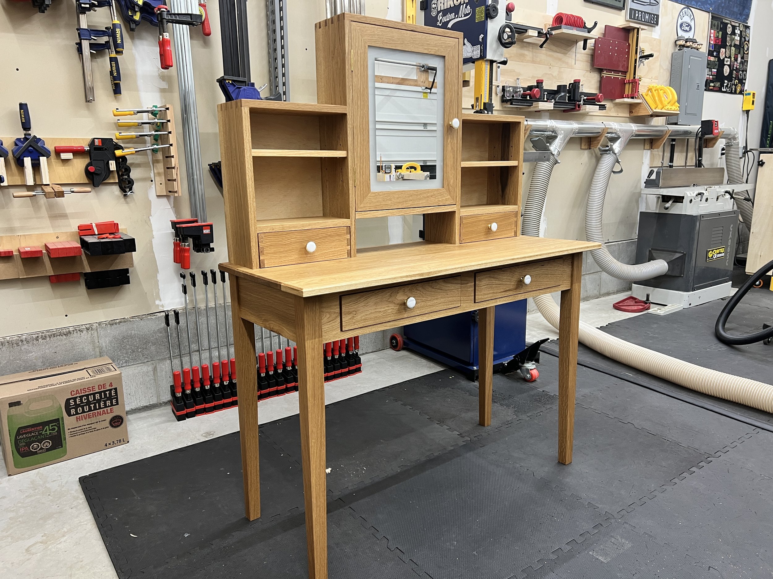 A woodworking workshop with a wooden cabinet, various clamps, and woodworking tools on a pegboard wall.