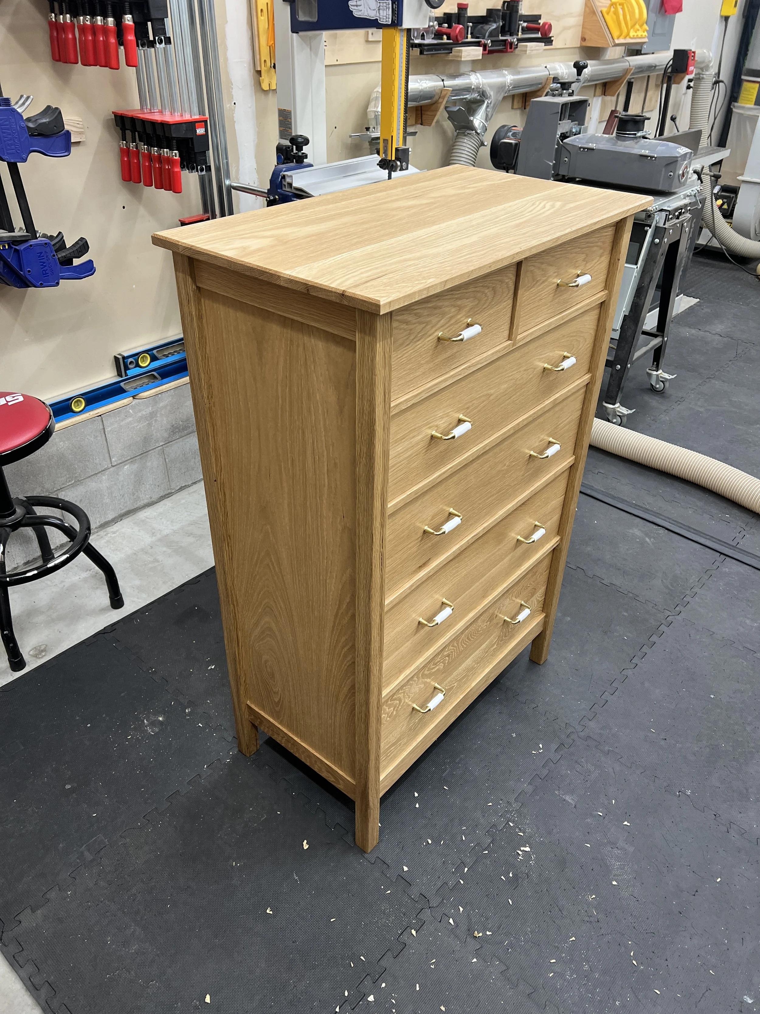 A wooden dresser with six drawers, sitting in a woodworking workshop, surrounded by tools and equipment.