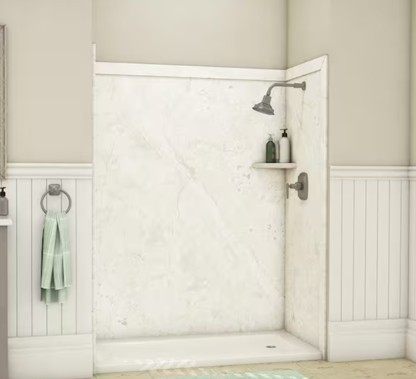 Empty walk-in shower with white marble walls, a wall-mounted showerhead, a small shelf with shampoo bottles, and a towel ring with a green towel nearby.