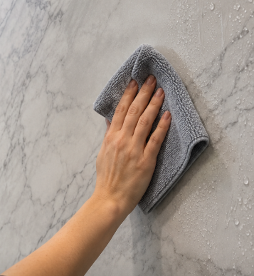 A hand wiping water off a gray marble surface with a gray cloth.