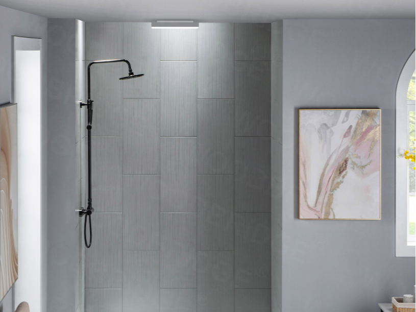 A modern bathroom shower with gray tiled wall, black shower head, and a framed abstract art piece on the wall next to a window.