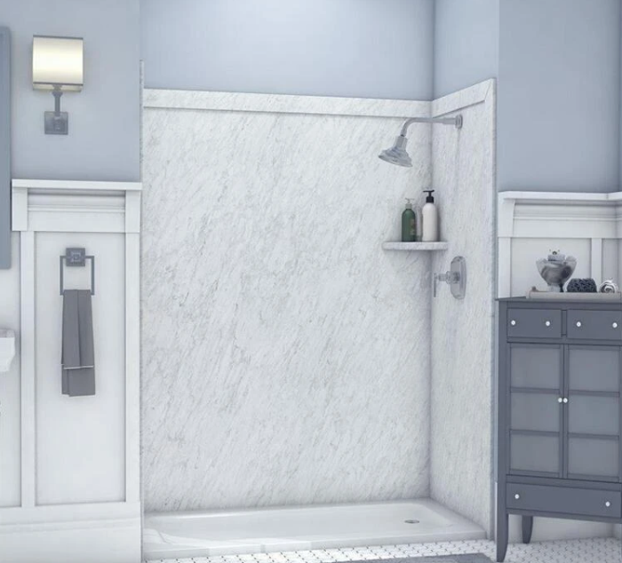 Bathroom shower with marble wall, showerhead, shelf with soap and shampoo bottles, towel rack with a towel, gray cabinet with accessories, and wall-mounted light.