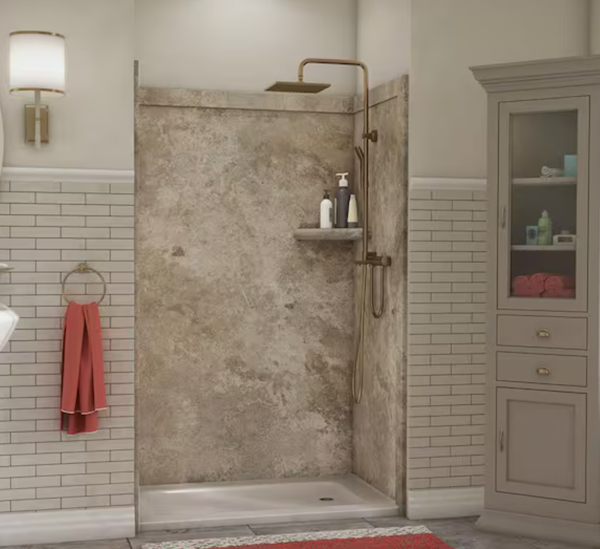 A modern bathroom with a walk-in shower featuring a textured stone wall, gold fixtures, and a small shelf with bottles. To the right, a light gray cabinet with glass doors holds towels, toiletries, and a green bottle. A wall-mounted light fixture and a towel ring with a pink towel are also visible.