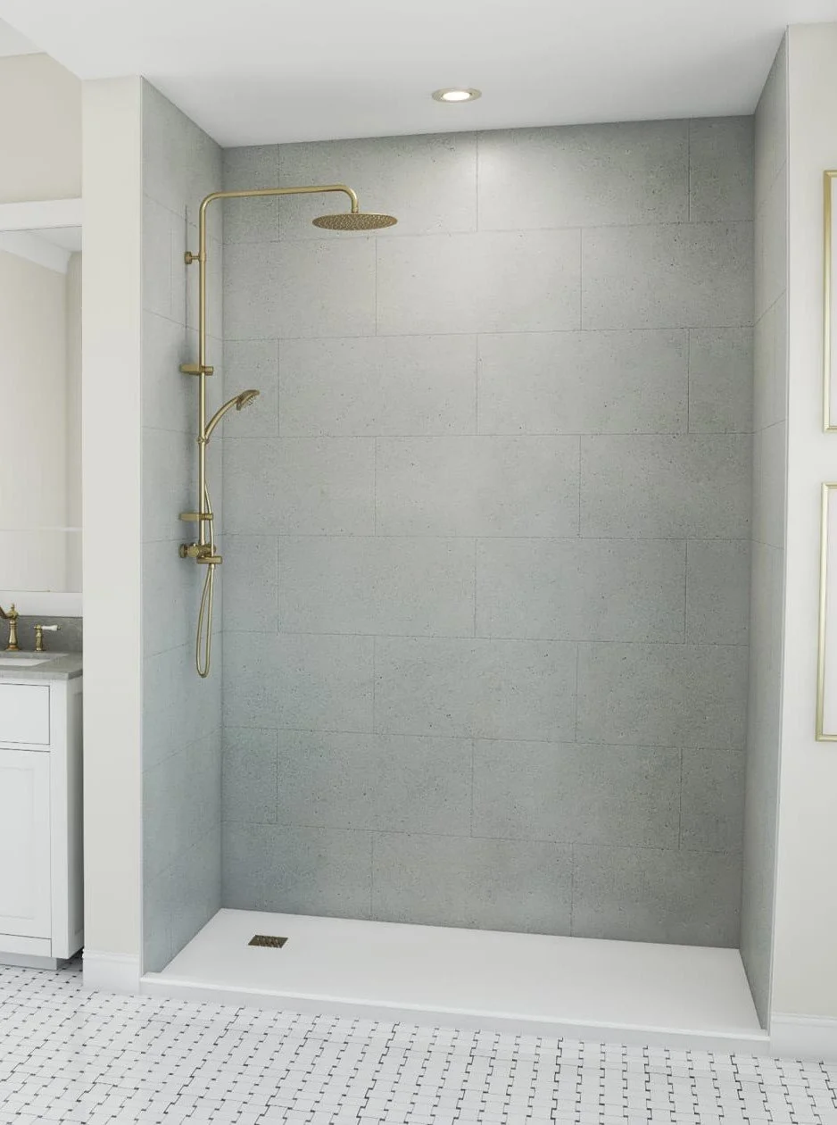 A modern, minimalist walk-in shower with gray tiled walls, a gold showerhead, and handheld shower fixture. The shower area has no door, and the flooring is white with small black tiles. A small drain is located on the shower floor near the corner.