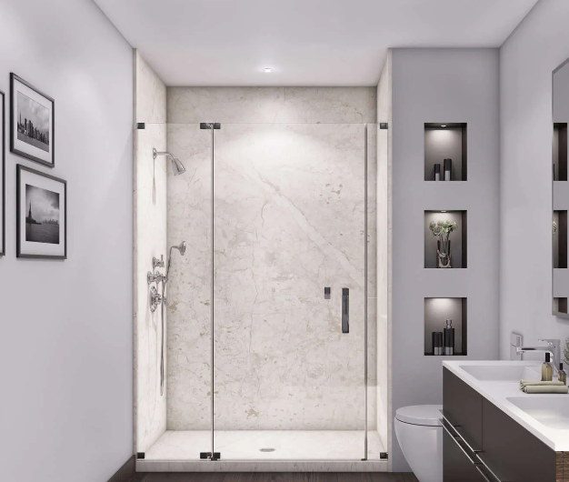 A bathroom shower area with white marble walls, a showerhead, and a small shelf holding shampoo and body wash bottles. A light blue towel hangs on a towel ring next to the shower, and a potted plant is placed on a gray cabinet nearby.