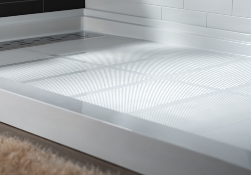 Close-up of a modern, white shower base with a textured surface, in a bathroom with white tiled walls.