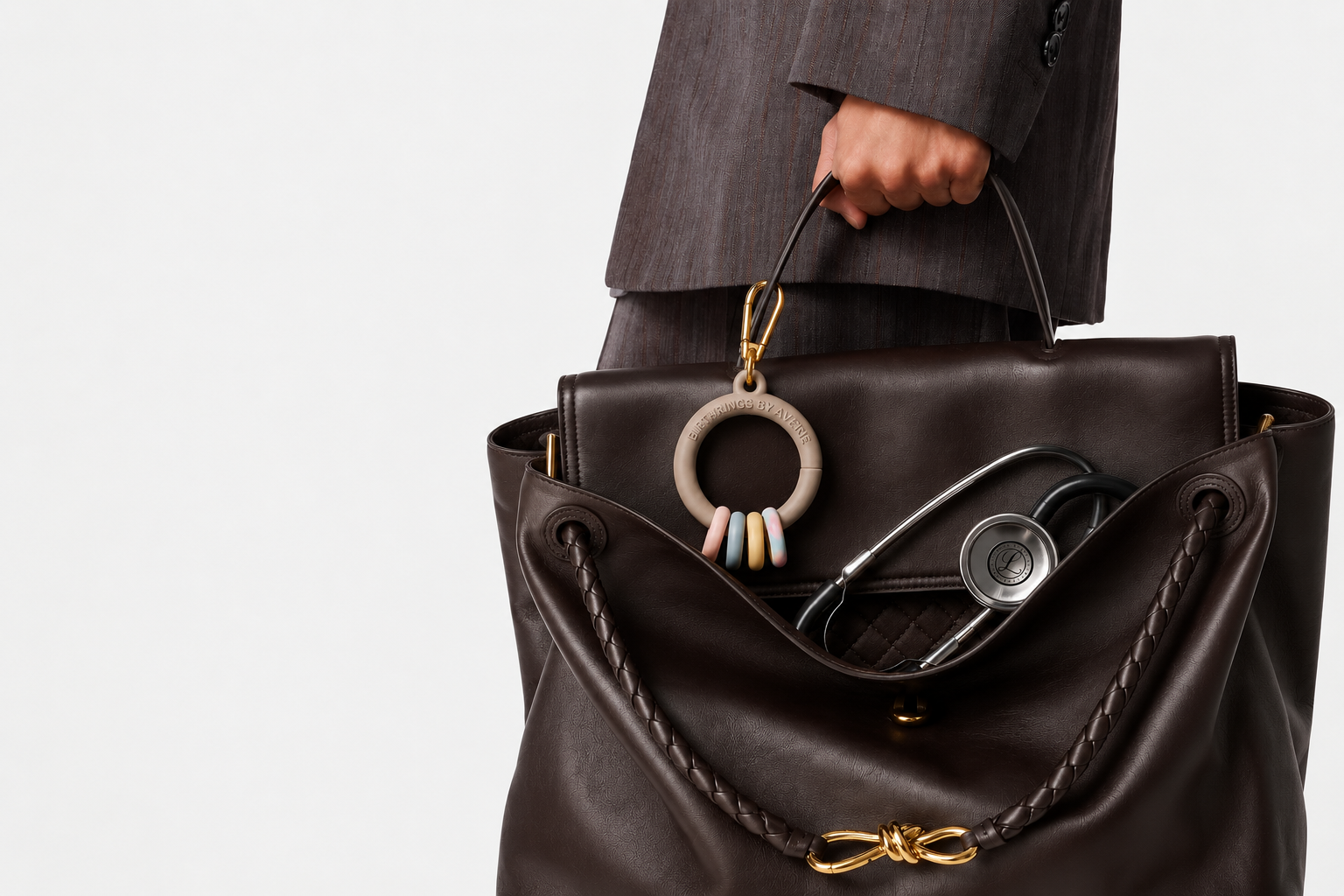 Person carrying a brown leather handbag with a stethoscope inside and a beige teething ring hanging from the handle.