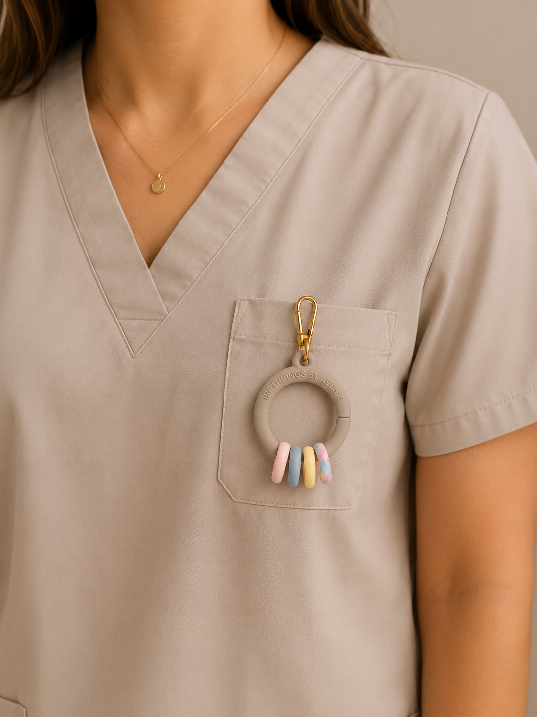Close-up of a woman wearing a beige nurse uniform with a gold necklace and a clay teething ring attached to her pocket.