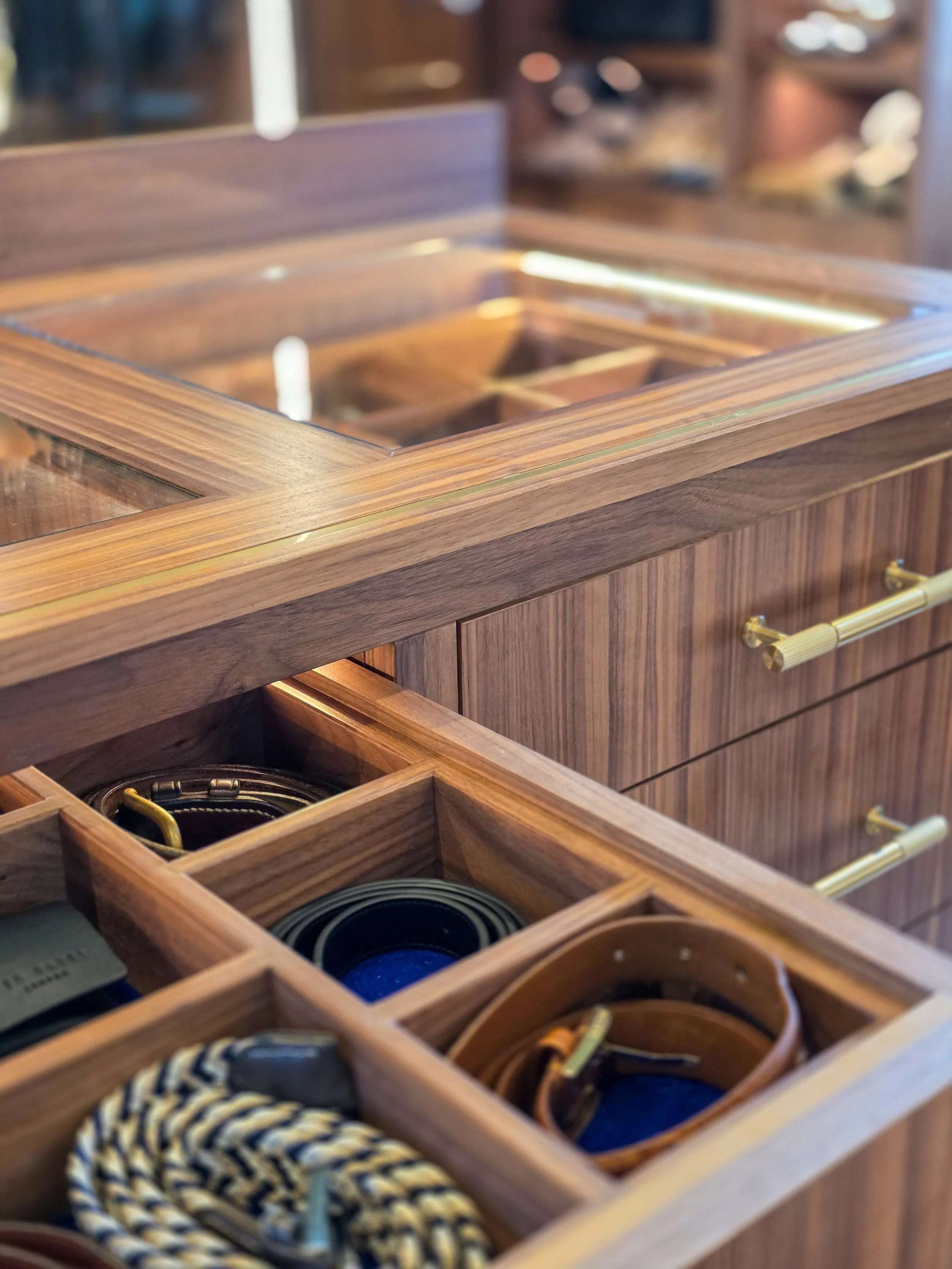 Open wooden drawer with compartments containing belts and other accessories.