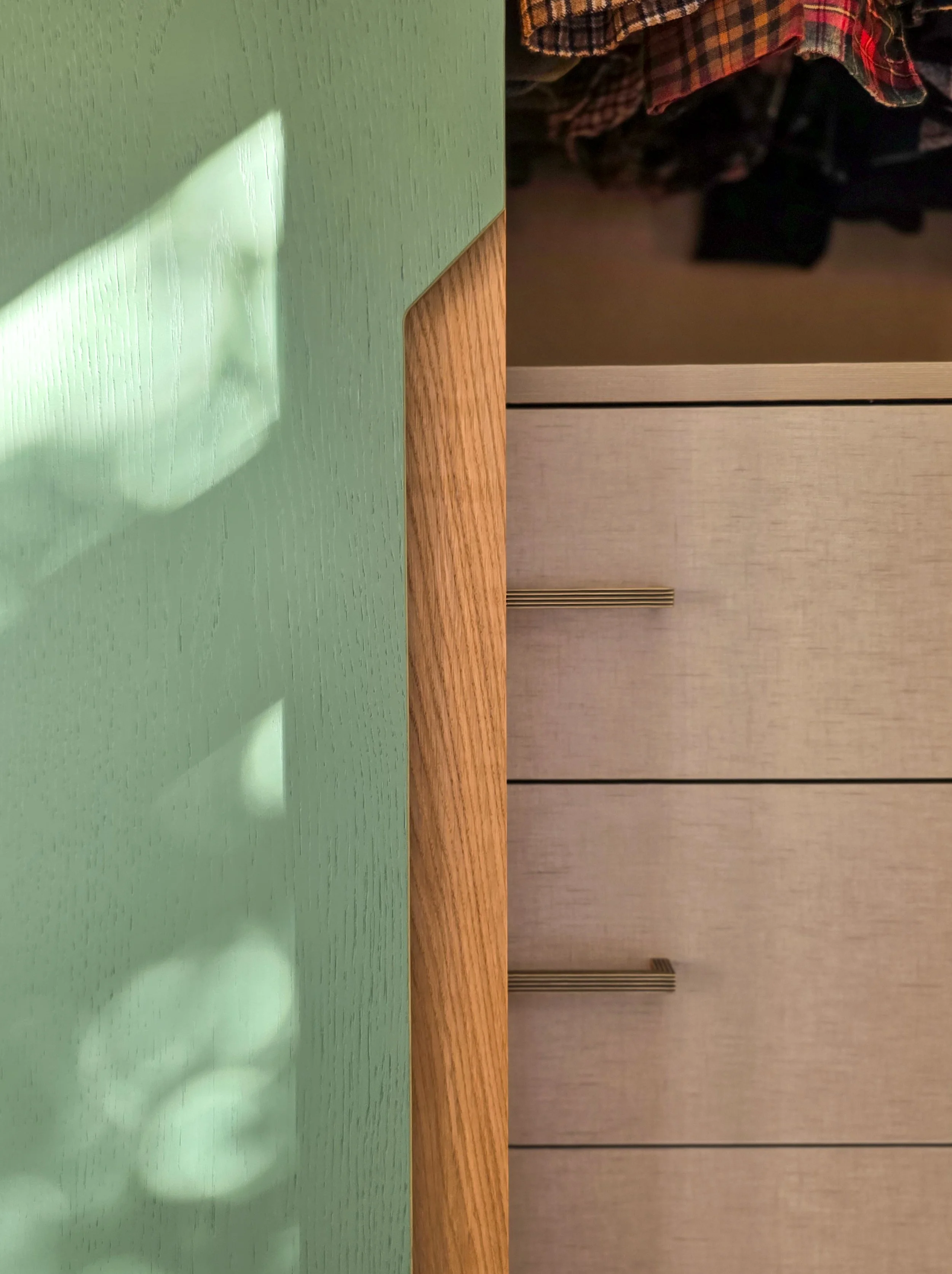 A shadow of a person taking a photo is cast on a green table, with a background of a beige wall and hanging clothing or fabric.
