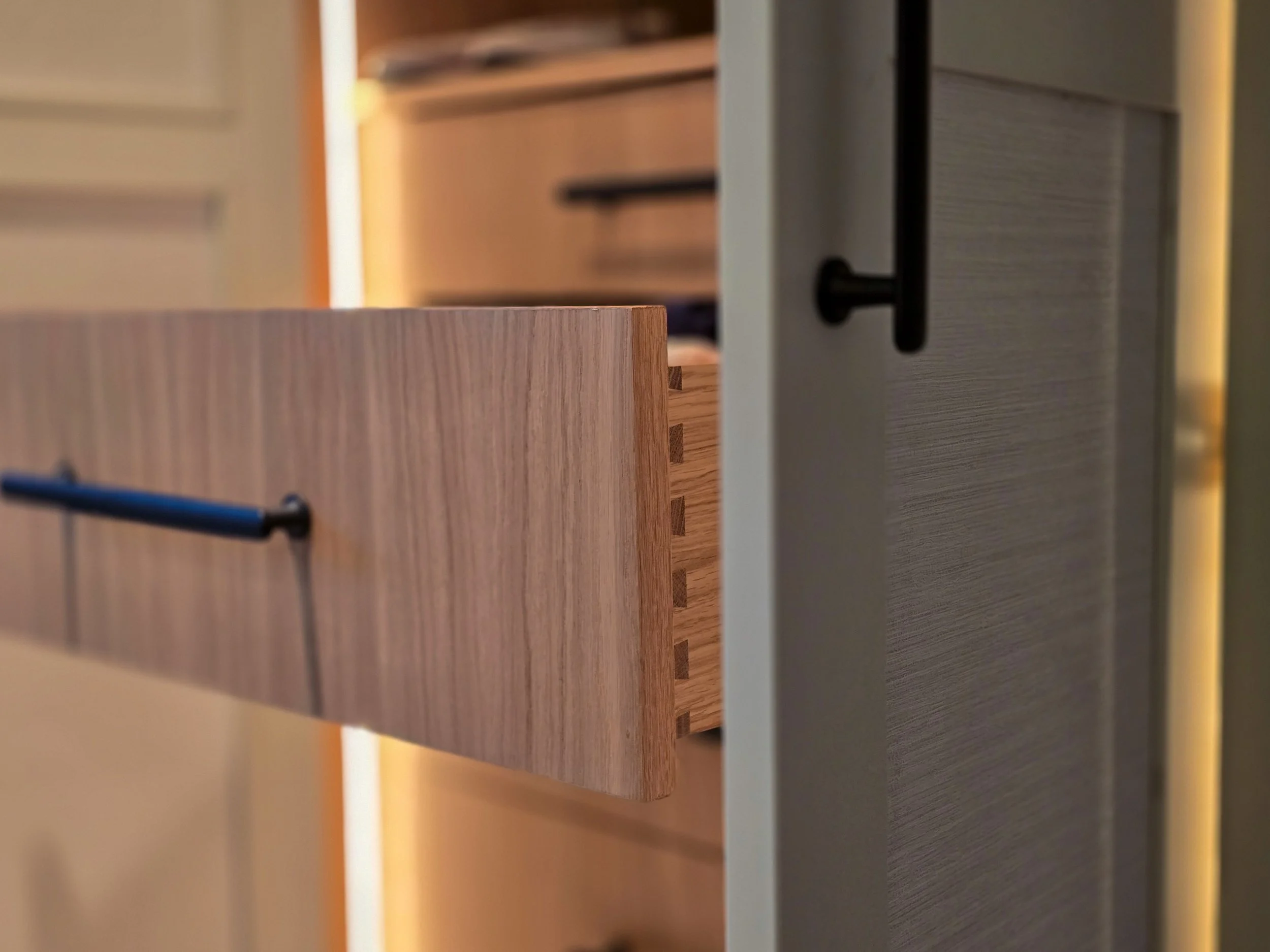 Close-up of wooden drawers and a white cabinet door with a black handle.