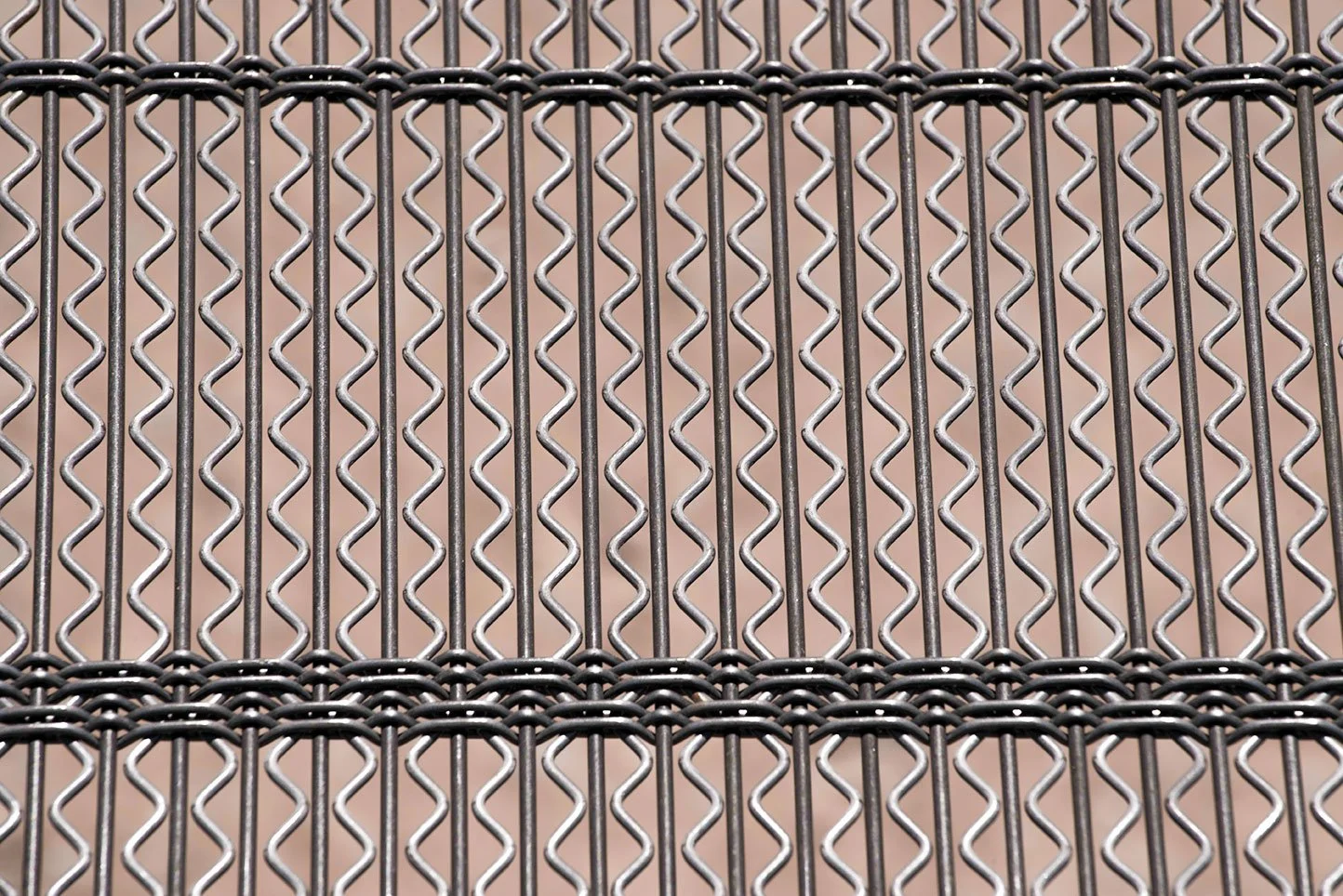 Close-up of a metal chain-link fence with a tan background.