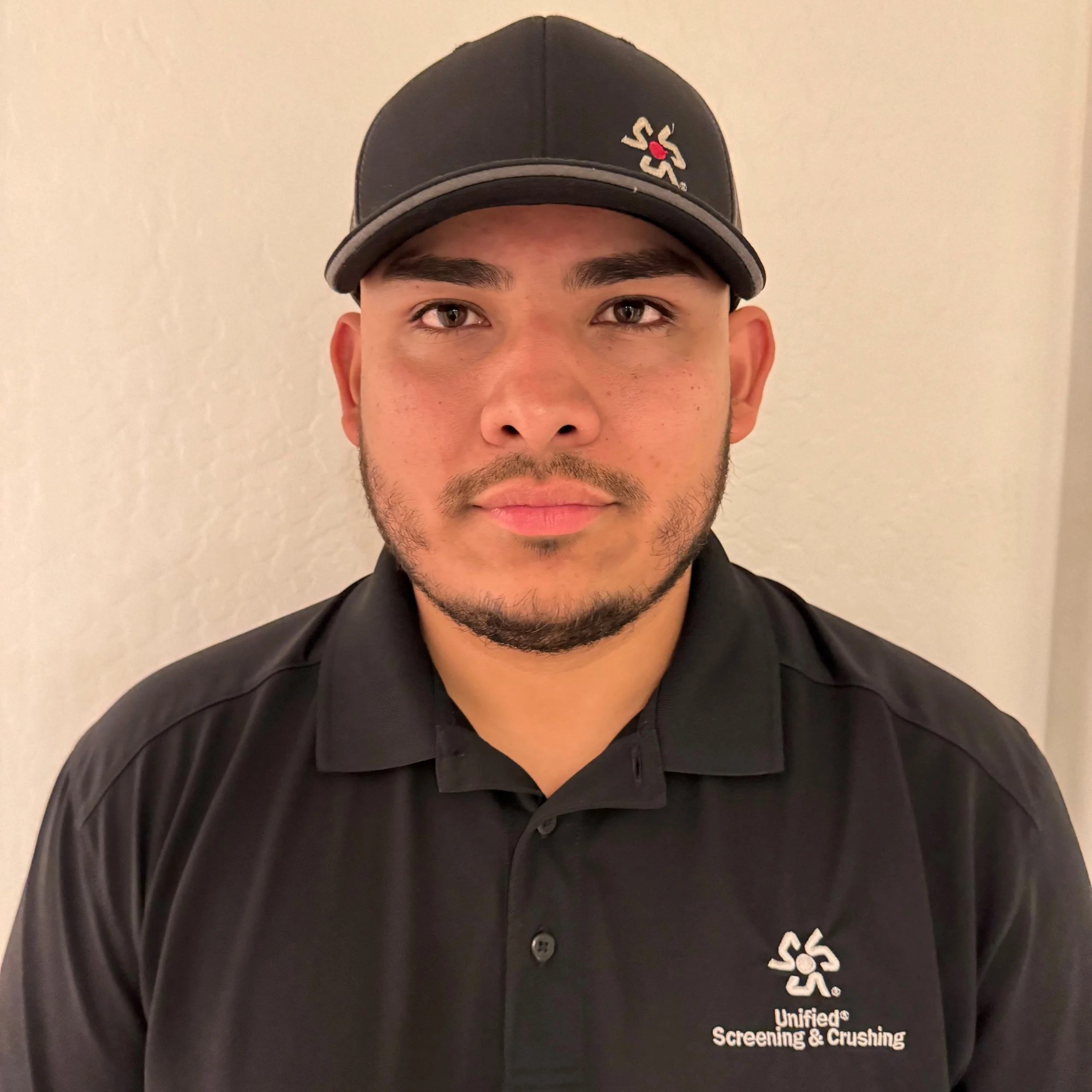 Close-up of a man wearing a black baseball cap and a black shirt with white embroidered text related to screening and crushing.