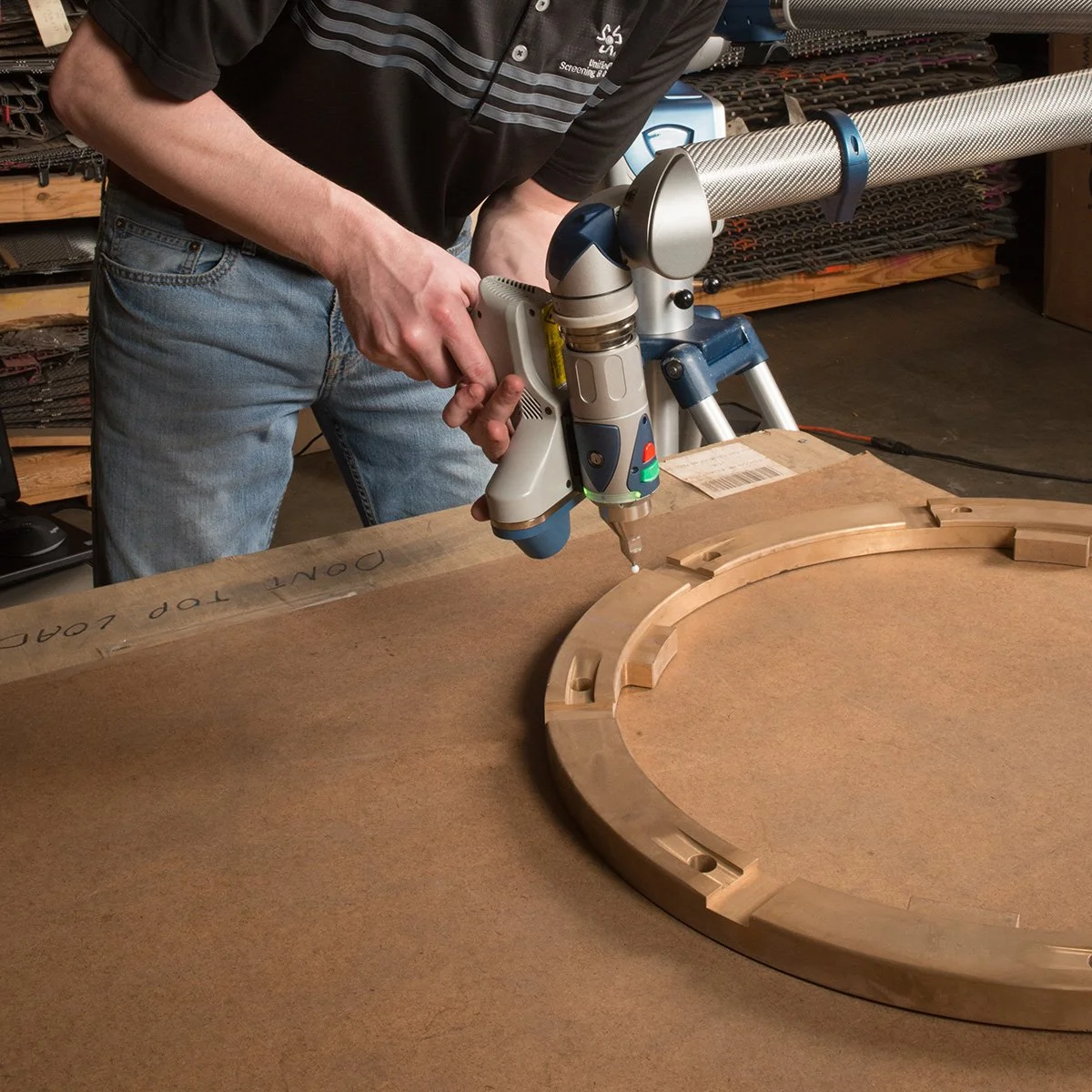 A person working on a woodworking project using a powered drill or screw gun to assemble a wooden circular frame on a workshop table.