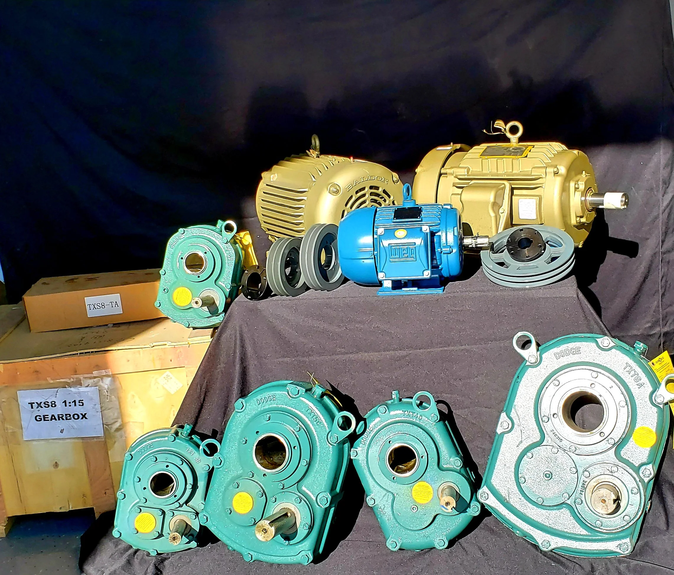 Various hydraulic gearboxes and motors displayed on a black cloth surface, labeled with tags 'TXS8-TA' and 'TXS8 1:15 GEARBOX'.
