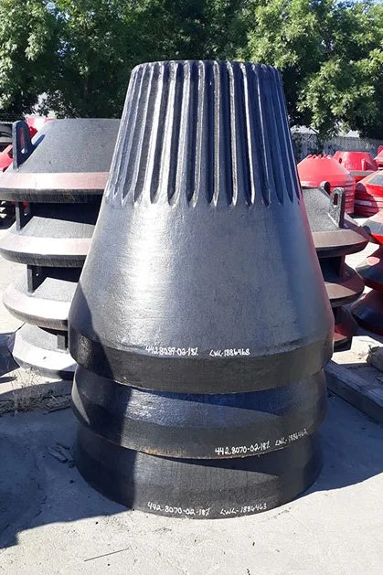 Large black industrial cone-shaped structure with vertical ridges at the top, situated outdoors with trees in the background and other similar equipment around.