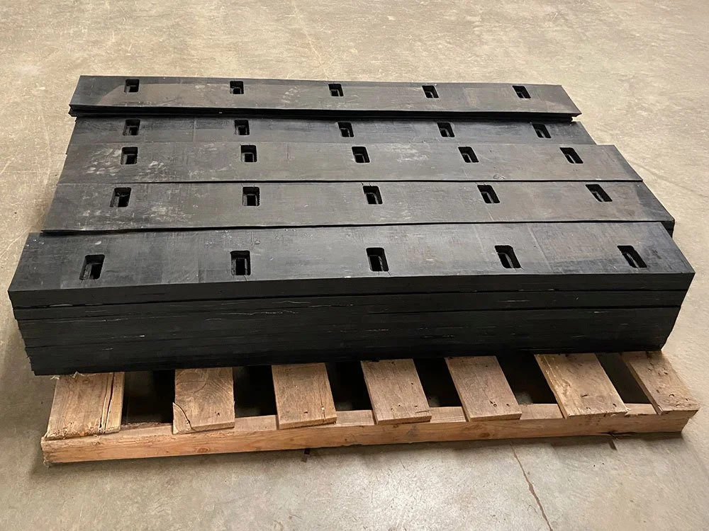 A stack of black rubber conveyor belt segments with rectangular cutouts on a wooden pallet.