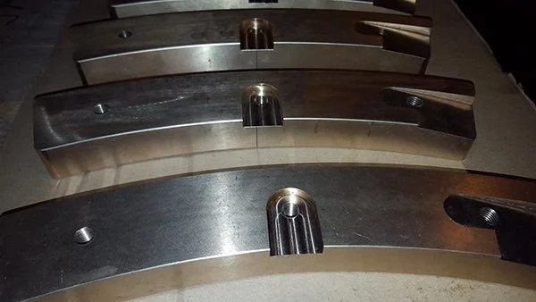 Close-up of three metallic objects aligned, each with a cylindrical protrusion in the center and a threaded hole on the side.