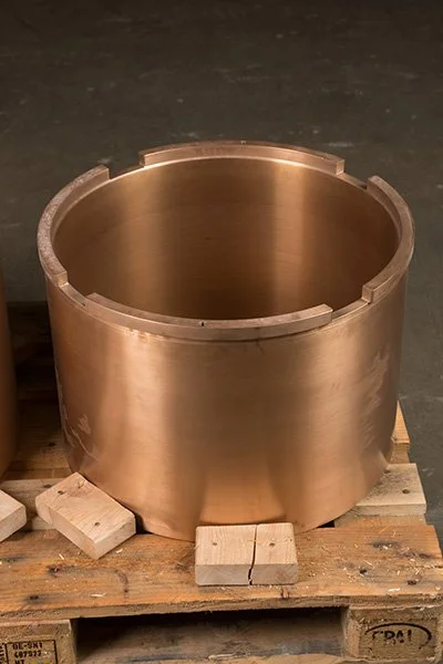 A large, cylindrical metal component with a smooth brushed finish, placed on wooden blocks on a pallet.