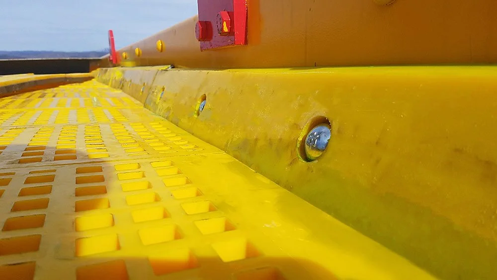 Close-up of a urethane pannel with a textured surface, screws, and a yellow, orange, and red structure in the background.