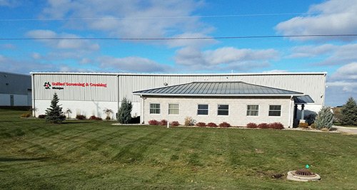 Large industrial building with a lawn in front and a blue sky with clouds above.