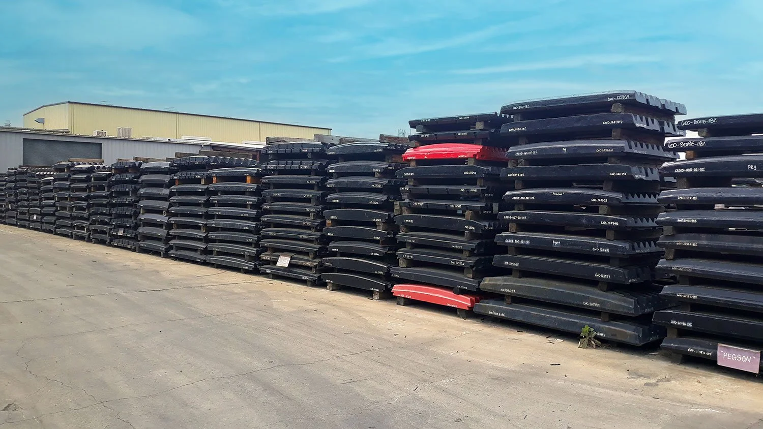 Large outdoor storage lot with multiple stacks of black plastic boat or trailer parts, some labeled, under a blue sky.