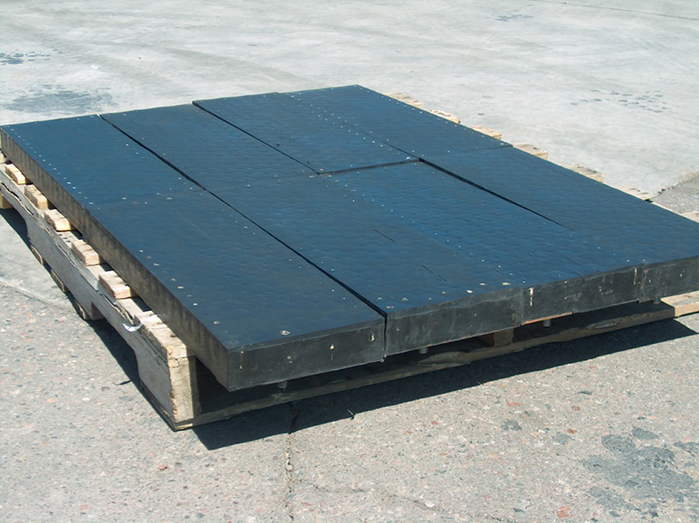 Black plastic pallets stacked on a wooden pallet outdoor on concrete ground.